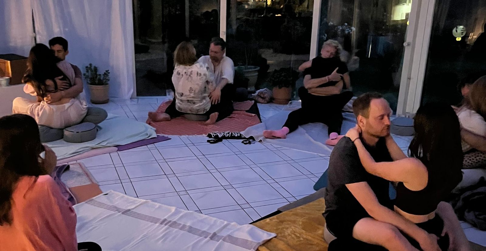 Mehrere Paare sitzen in einem Wintergarten bei Kerzenlicht und halten sich.